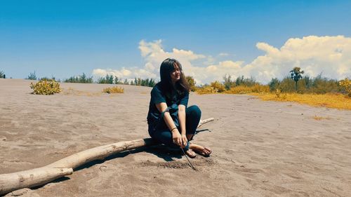 Young woman sitting on land against sky