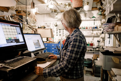 Side view of senior saleswoman using computer while standing at checkout in hardware store