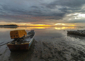 Boat moored on beach against sky during sunset