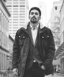 Portrait of young man standing against buildings in city