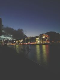 Illuminated city by river against sky at night