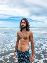 Young man standing at beach against sky