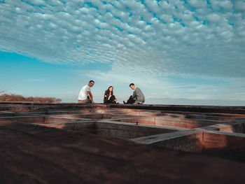 Friends sitting on wooden built structure against blue sky