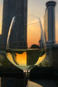 Close-up of wineglass against modern buildings during sunset