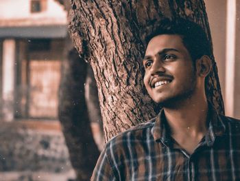Portrait of smiling young man against tree trunk