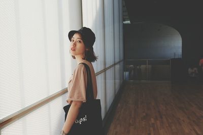 Side view of young woman standing against window