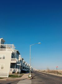 Road by buildings against clear blue sky