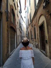 Rear view of woman standing on footpath amidst buildings