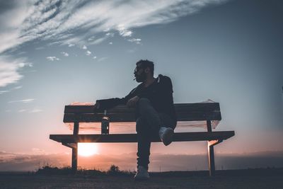 Man sitting on bench in park during sunset