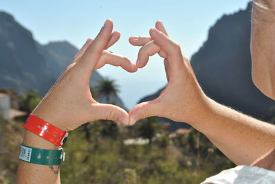 Cropped hands of man making heart shape against sky