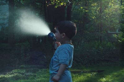 Side view of boy holding garden hose at yard