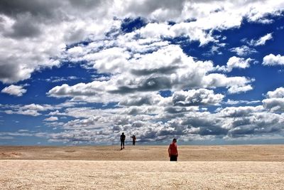 People walking at beach against cloudy sky