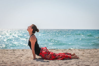 Side view of young woman on beach against clear sky