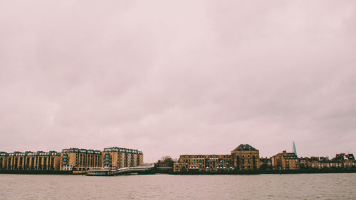 Buildings at waterfront against cloudy sky