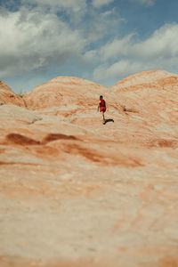 Solo female hiker walks up a petrified sand dune in red rocks of utah