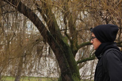 Side view of young woman standing by bare tree in forest