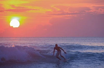 Full length of teenage boy surfing in sea against sky during sunset