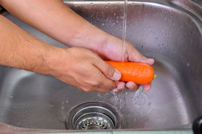 Cropped image of hands cleaning carrot in kitchen sink