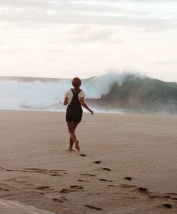 Rear view of woman on beach against sky