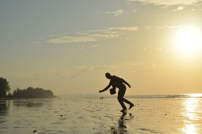 Silhouette man on beach against sky during sunset