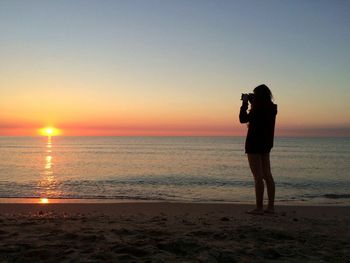 Woman photographing sea during sunset