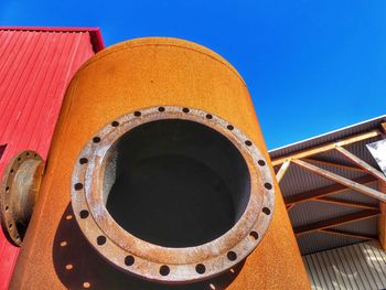 Low angle view of rusty wheel against clear blue sky