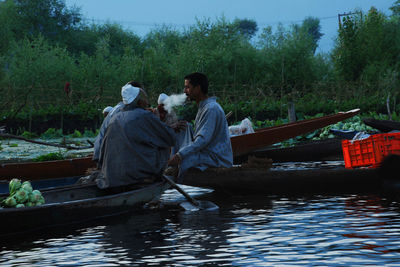 Men sitting on riverbank against trees