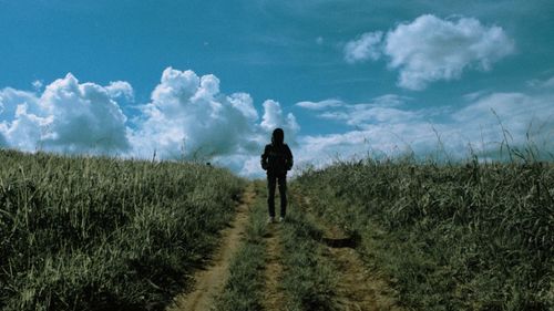 Rear view of man walking on field against sky