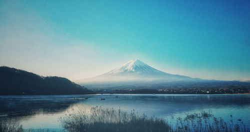 Scenic view of lake by snowcapped mountains against clear blue sky