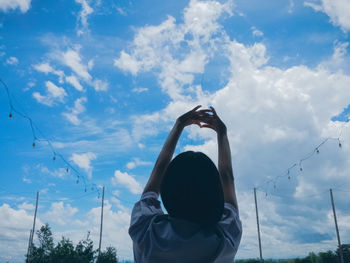 Rear view of woman with arms raised standing against cloudy sky