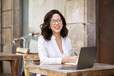 Young woman using her laptop on the terrace in a bar, having some notes.