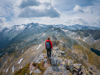 Rear view of woman hiking on rocky mountain peak against sky