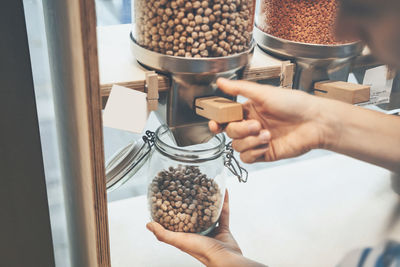 Hands of woman filling chickpeas in jar at convenience store