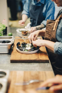 Midsection of chefs preparing food in plate on counter at restaurant kitchen