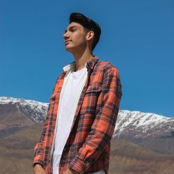 Young man standing on mountain against clear blue sky