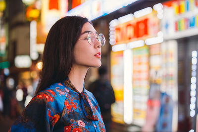 Portrait of woman looking away while standing against store