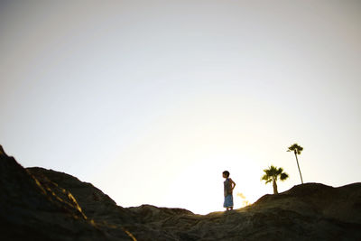 Low angle view of boy standing on rock formations against clear sky at laguna beach