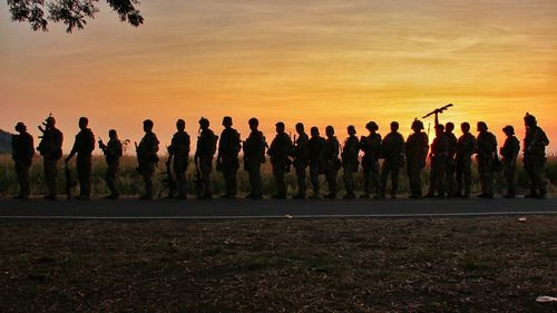 Army soldiers standing on road against sky during sunset