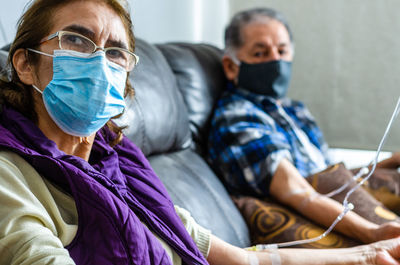 Senior couple wearing mask sitting at hospital