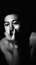 Close-up of thoughtful shirtless young woman against black background