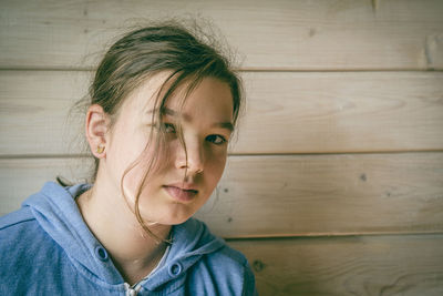 Close-up portrait of young woman against wooden wall