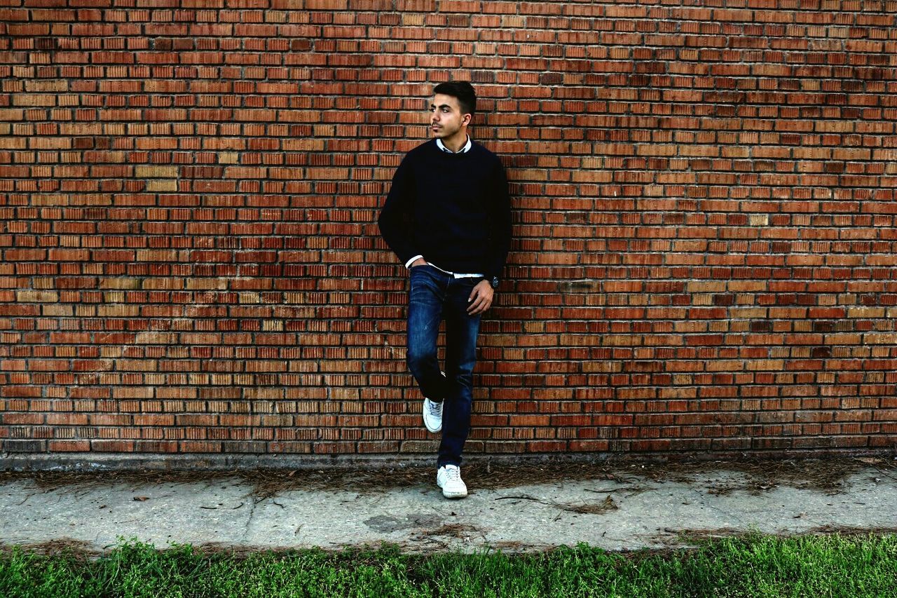 brick, brick wall, one person, full length, wall, standing, architecture, wall - building feature, lifestyles, casual clothing, real people, built structure, looking at camera, front view, leisure activity, portrait, young adult, building exterior, young men, outdoors, jeans, contemplation