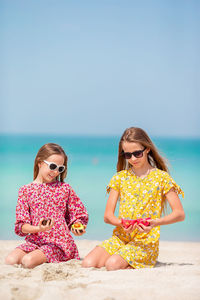 Girls holding fruit while kneeling at beach