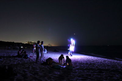 People enjoying at beach against clear sky at night