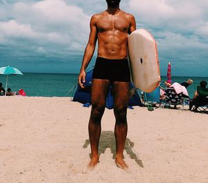 Full length of shirtless man standing on beach against sky