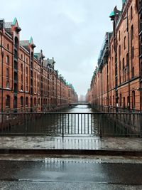 Wet street amidst buildings against sky during rainy season