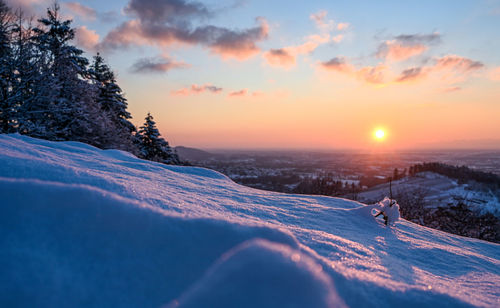 Snow covered landscape against sky during sunset