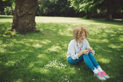 Full length of girl sitting on grass against trees