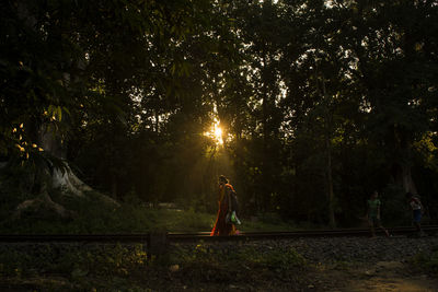 Side view of woman walking against trees in forest at sunset