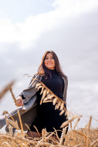 Low angle view of smiling young woman standing amidst plants against cloudy sky